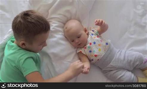 Boy with junior baby sister at home. Child holding brothers fingers. Lovely siblings