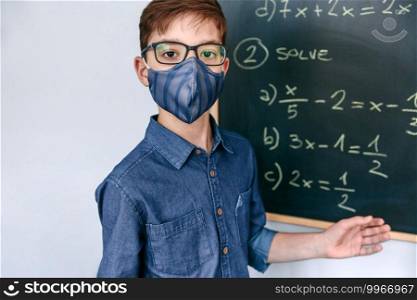 Boy with mask in front of a blackboard with equations at school
