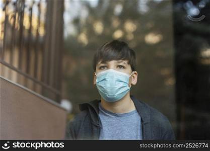 boy with medical mask looking outside window
