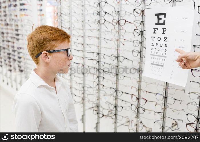 boy with spectacle looking snellen chart while doctor s hand pointing chart