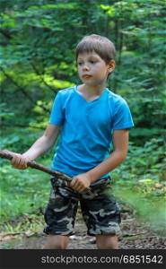 Boy with wooden stick in summer forest park