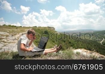 boy working on his laptop on the edge of the cliff in the mountains