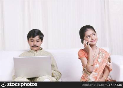 Boy working on laptop while girl talks on mobile phone