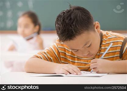 Boy writing on a notepad in a classroom