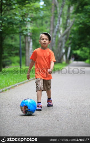 Boy young kid playing with ball kicks running towards ball in park outdoors