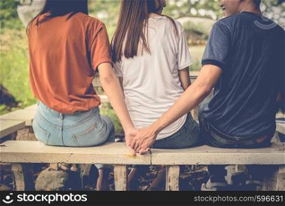 Boyfriend and another woman grab hands from behind together without sight of his girlfriend.. Paramour and divorce concept. Social problem and cheating couples theme. Teen adult and University theme.