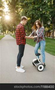 Boyfriend teaches his girl to ride on gyro board in summer park. Outdoor recreation with electric gyroboard. Transport with balance technology. Boyfriend teaches his girl to ride on gyro board