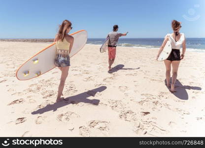 Boys and girls teen surfers with surfboards walking at a sandy beach.