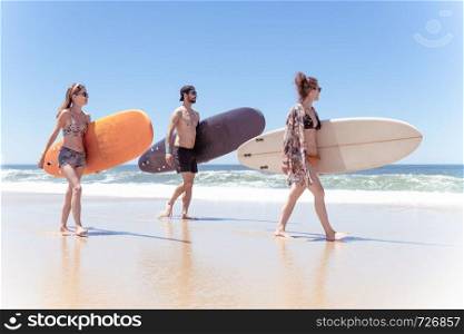 Boys and girls teen surfers with surfboards walking at a sandy beach.