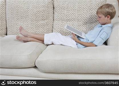 Boys sits on sofa reading a digital book
