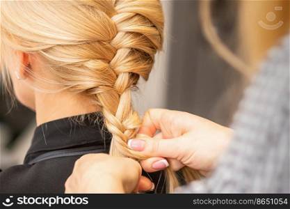 Braiding braid. Hands of female hairdresser braids long braid for a blonde woman in a hair salon. Braiding braid. Hands of female hairdresser braids long braid for a blonde woman in a hair salon.