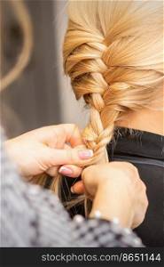 Braiding braid. Hands of female hairdresser braids long braid for a blonde woman in a hair salon. Braiding braid. Hands of female hairdresser braids long braid for a blonde woman in a hair salon.
