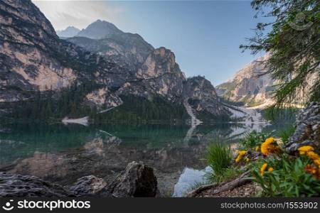 Braies Lake and its reflections seen from a beach between rocks and tree roots, Italian landscape in South Tyrol