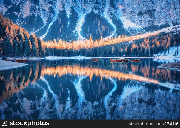 Braies lake with beautiful reflection in water at sunrise in autumn in Dolomites, Italy. Landscape with forest, mountains, boats on the lake, water, trees with colorful foliage. Italian alps. Nature
