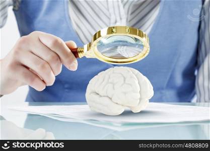 Brain research and education concept. Close view of woman zooming human brain with magnifying glass