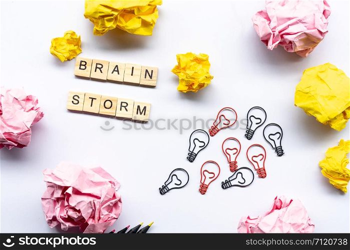 Brainstorm concept word on wooden block surrounded by crumpled papers and light bulb paperclip