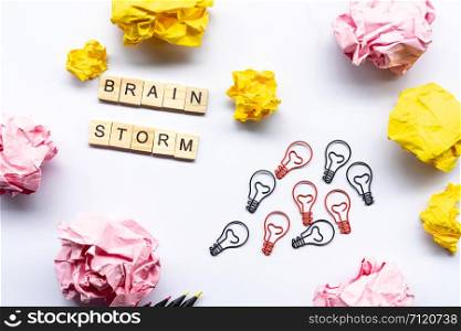 Brainstorm concept word on wooden block surrounded by crumpled papers and light bulb paperclip