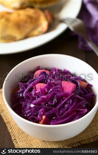 Braised Red Cabbage. Braised red cabbage with apple in bowl, with roasted chicken thigh in the back, photographed with natural light (Selective Focus, Focus in the middle of the dish)