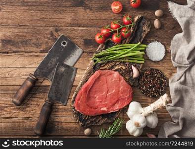 Braising steak on chopping board with rosemary, asparagus and tomatoes with salt and pepper with rosemary and meat hatchets on wooden background. Best meat for barbeque