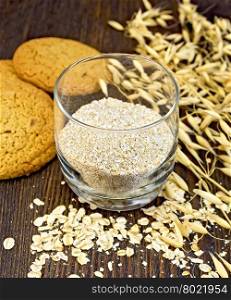 Bran small oat in a two glassful, oatmeal and ears, cookies on a background of wooden boards