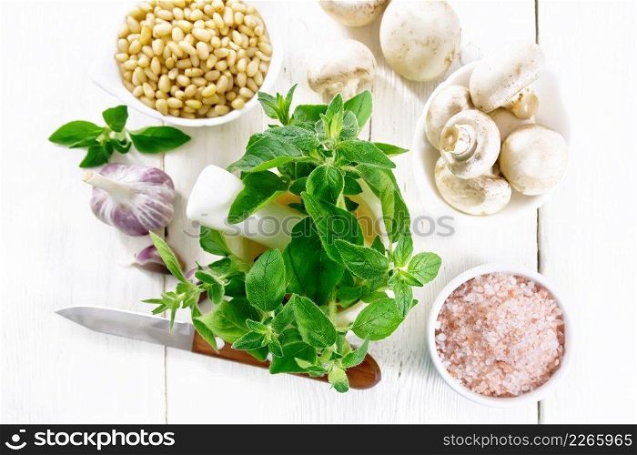 Branches of fresh oregano with leaves in a mortar, ch&ignons, pink Himalayan salt, pine nuts, garlic and a knife on wooden board background from above