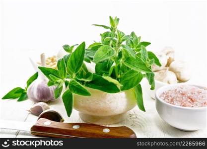 Branches of fresh oregano with leaves in a mortar, ch&ignons, pink Himalayan salt, pine nuts, garlic and a knife on wooden board background 