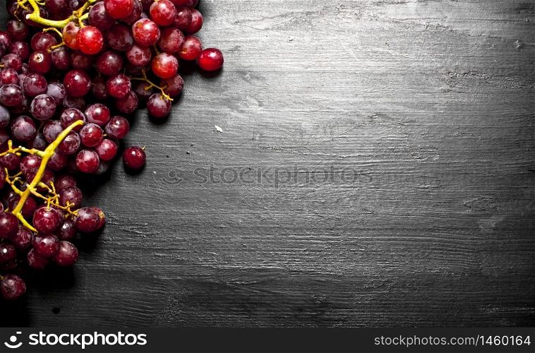 Branches of red grapes . On a black wooden background.. Branches of red grapes .