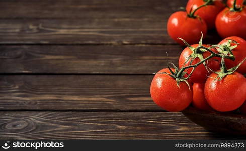 Branches of ripe juicy tomatoes on a dark wooden background. Fresh tomatoes close-up with copy space. Tomatoes in drops of water.