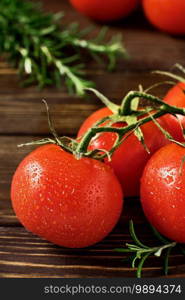 Branches of ripe red tomatoes and branches of rosemary on dark wooden background. Close-up, selective focus. Tomatoes in drops of water. Natural fresh food from the market to prepare the best dishes