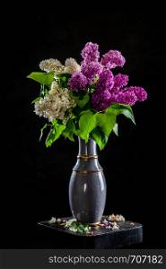 Branches of white and purple lilac in vase on black background. Spring branch of blooming lilac on the table with black background. Fallen lilac flowers on the table.