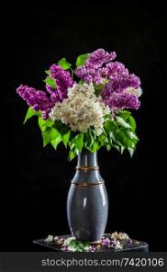 Branches of white and purple lilac in vase on black background. Spring branch of blooming lilac on the table with black background. Fallen lilac flowers on the table.
