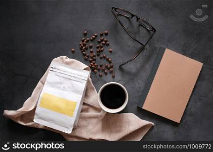 Branding identity of coffee beans and hot cup of black coffee drink with blank notebook on stone background, business and mockup concept