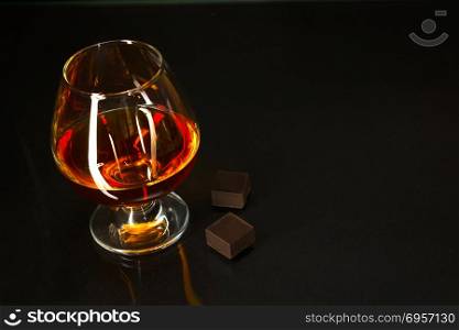 Brandy glass and chocolate on black background. Brandy glass. Cognac glass. Whiskey glass. Cognac france.. Brandy glass and chocolate on black background