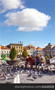 BRASOV, ROMANIA - NOVEMBER 01, 2017: family feeding pigeons on a main square of romanian town Brasov at 01, 2020