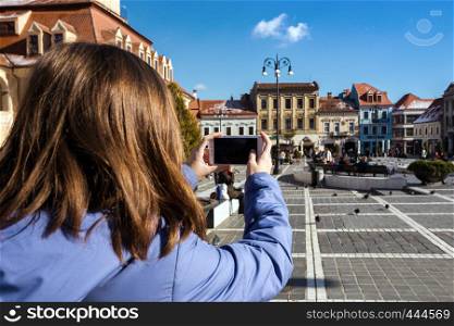 BRASOV, ROMANIA NOVEMBER 1, 2017: view of the main square at the Brasov and girl taking a photo on a smartphone. BRASOV, ROMANIA, November 1, 2017