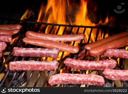 Brats cooking on the grill with a flame in the background