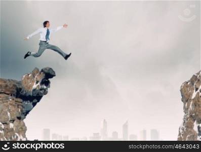 Brave businessman. Young businessman in suit jumping over mountain gap