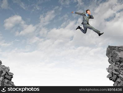 Brave businessman. Young businessman in suit jumping over mountain gap