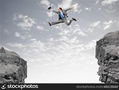 Brave businessman. Young businessman with suitcase jumping over mountain gap
