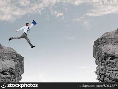 Brave businessman. Young businessman with suitcase jumping over mountain gap