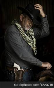 Brave cowboy Handsome old man wearing grey clothes white gun green fabric and catch black hat looking at camera while standing against dark background