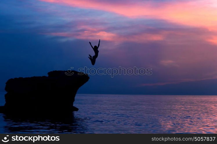 Brave girl jumping from the rocks in the evening on beautiful purple sunset background, summer adventure, freedom concept