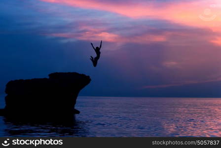 Brave girl jumping from the rocks in the evening on beautiful purple sunset background, summer adventure, freedom concept