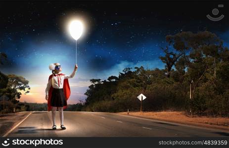 Brave superkid. Cute girl of school age in superhero costume with balloon in hand