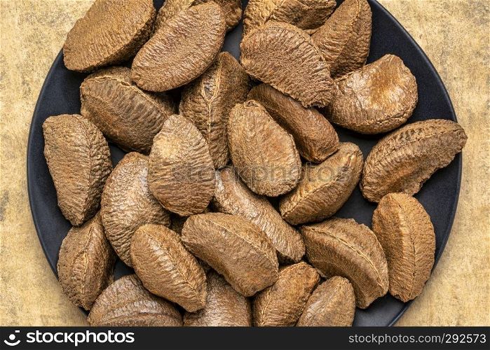 Brazilian nuts on a black plate against buckskin textured paper background with a copy space