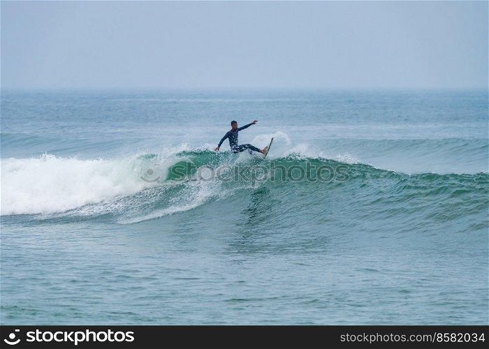 Brazilian surfer in action in the waves of the Atlantic coast of Portugal. On a cloudy morning at Furadouro beach, Ovar - Portugal.