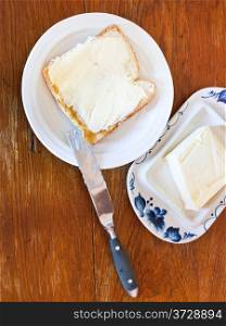 bread and butter sandwich on white plate, knife, dairy butter, butterdish on wooden table