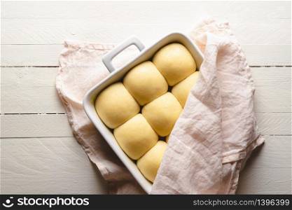 Bread buns uncooked in a white tray ready to be put in the oven. Above view with bread buns dough unbaked in an oven tray.