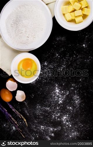 bread concept a bowl of raw egg, cubes of butter, flour put on the black scene with a sprinkle of flour on it.