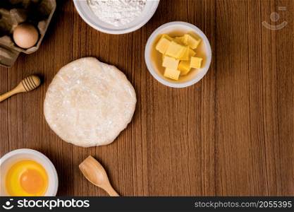 bread concept a bun dough, a tiny wooden spatula, a bowl of flour and a bowl of a raw egg organized on the wooden scene.